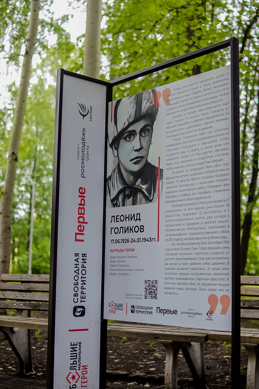 Установленный стенд с историей Лёни Голикова среди деревьев в ОК «Саулык»